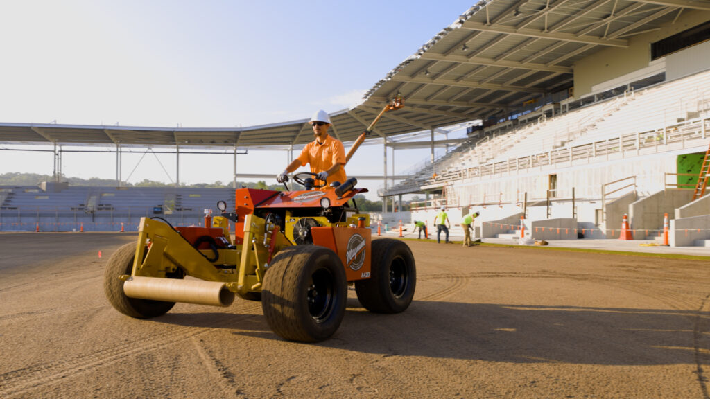 A man rides an A-Series installer for sports turf management.