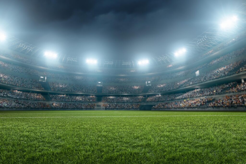 A close up look at grass in a stadium packed with people at night with the lights on after a recent field construction project.